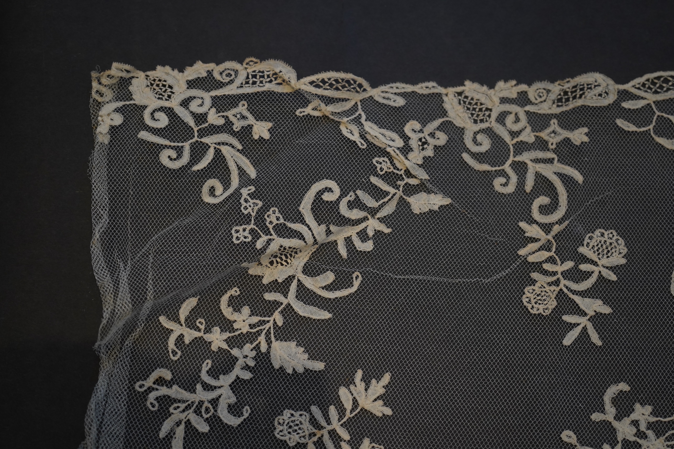 A 19th century five yard flounce of Brussels bobbin appliqué lace applied onto fine machine net, worked in a trailing floral design with an ornate border and sprig motifs, 457.5 cm long x 36cm deep. Condition - possibly